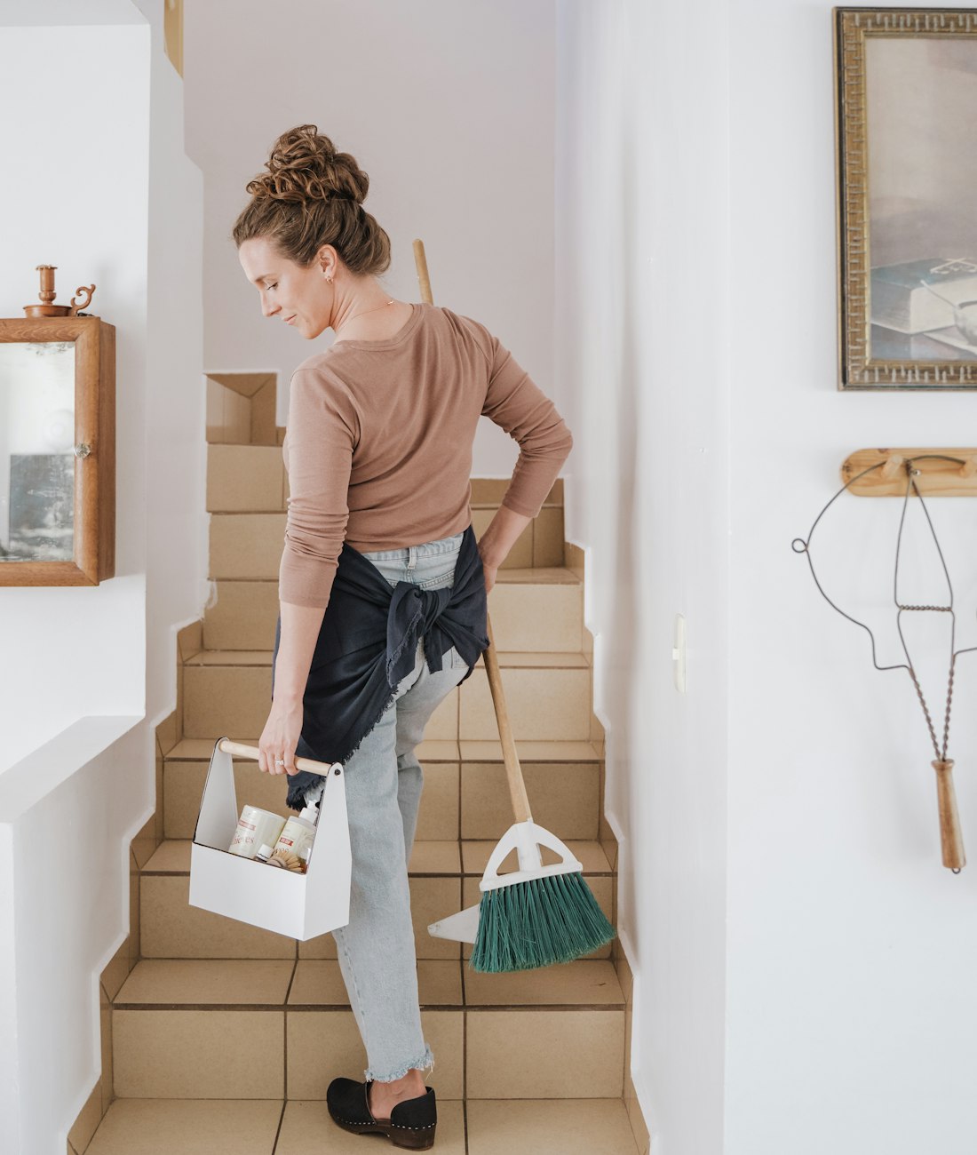 Busy Bees cleaner carrying a cleaning caddy and broom up the stairs of a home